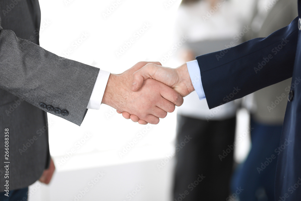 Business people shaking hands at meeting or negotiation, close-up. Group of unknown businessmen and women in modern office at background. Teamwork, partnership and handshake concept