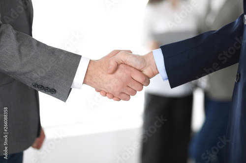 Business people shaking hands at meeting or negotiation, close-up. Group of unknown businessmen and women in modern office at background. Teamwork, partnership and handshake concept © rogerphoto
