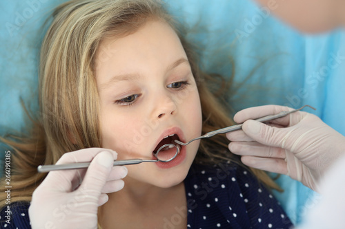 Little baby girl sitting at dental chair with open mouth and feeling fear during oral check up while doctor. Visiting dentist office. Medicine concept