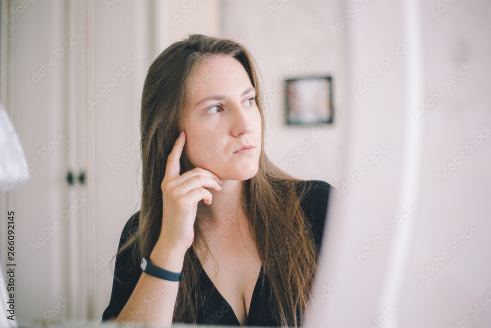 Close-up girl of European appearance thoughtfully sits in front of a mirror in a bright hotel room Close-up girl of European appearance thoughtfully sits in front of a mirror in a bright hotel room