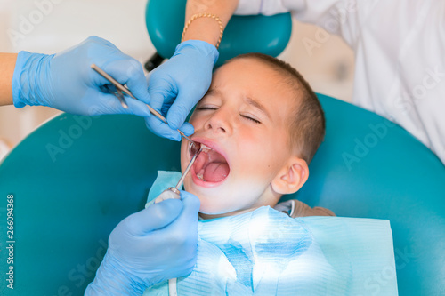 Dentist is treating a boy s teeth. Dentist examining boy s teeth in clinic. A small patient in the dental chair smiles. Dantist treats teeth
