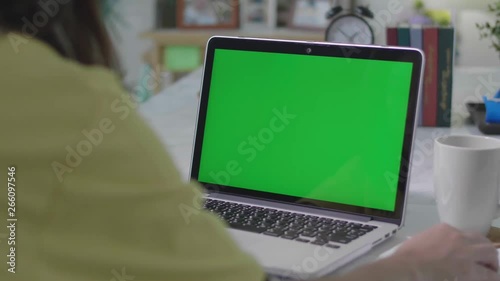 Woman working on the laptop computer with green screen at home. Chroma key. View from the back. 