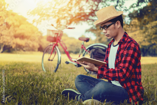 Portrait of handsome Asian man bearded wearing glasses reading a book at the park on a summer day. Education learning concept.