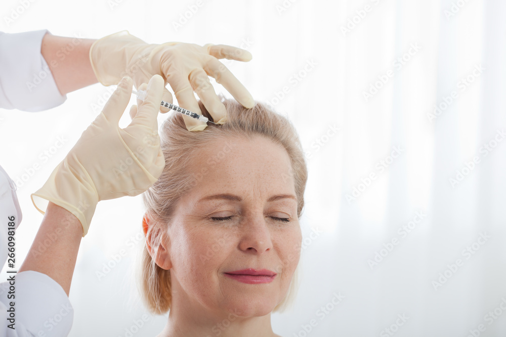 Naklejka premium Middle aged woman gets cosmetic injection in her forehead. Hyaluronic acid injection for facial rejuvenation procedure. Woman in beauty salon. Plastic surgery clinic.