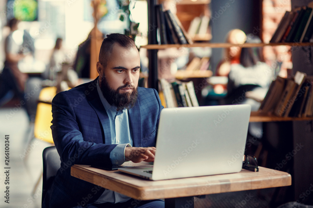 Businessman bearded man in a suit works behind the laptop sitting in a comfortable office coworking.