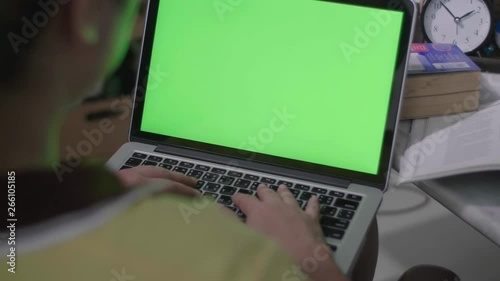 Woman working on the laptop computer with green screen at home. Chroma key. View from the back. 