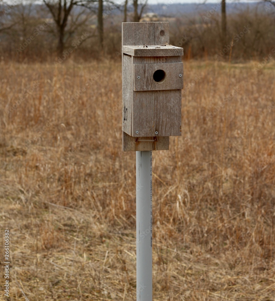 A old wooden birdhouse on the pole in the country field.