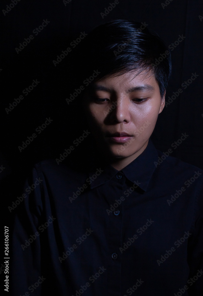 Studio portrait of a Thai Asian LGBT,women handsome beautiful young man  standing on black backdrop is black shirt with feeling on face.
