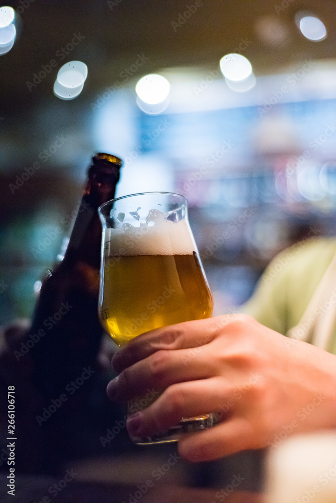 man's hand holds a bottle and glass of beer in bar