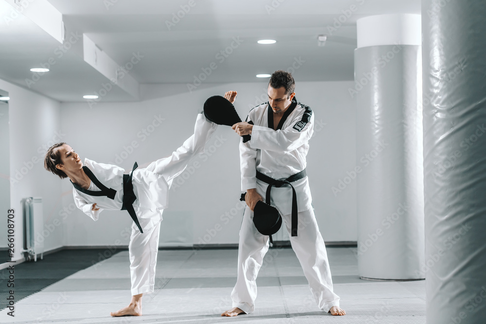 Fototapeta Caucasian handicapped highly motivated girl practicing taekwondo with her training. Girl kicking kick target.