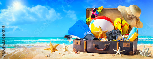 Beach accessories in suitcase on sand. Family holidays concept
