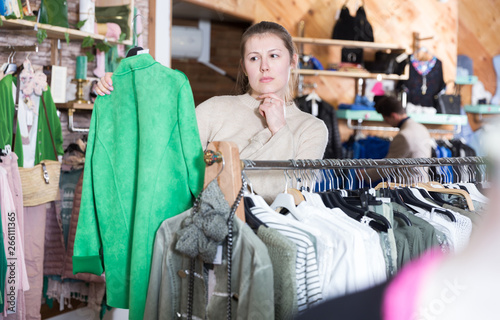 Smiling woman is choosing clothes and looking on green pullover