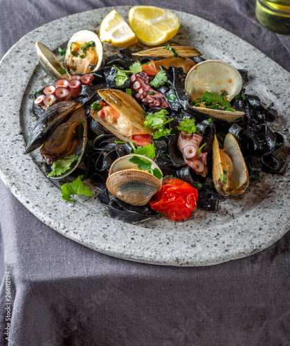 Seafood black fettuccine fehttuchini. Black pasta with squids, octopus clams, mussels on stone plate. Gourmet dish