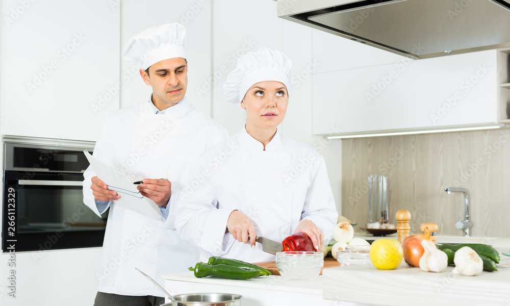 Cheerful woman and man young chefs preparing food with paper recipe