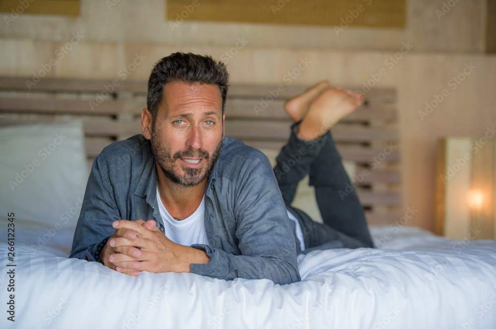 interior portrait of 30s to 40s happy and handsome man at home in casual shirt and jeans lying on bed relaxed at home smiling confident and happy feeling positive