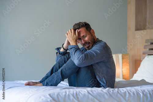 young attractive overwhelmed and depressed man sitting on bed worried and frustrated suffering depression crisis covering face with hands feeling desperate © TheVisualsYouNeed