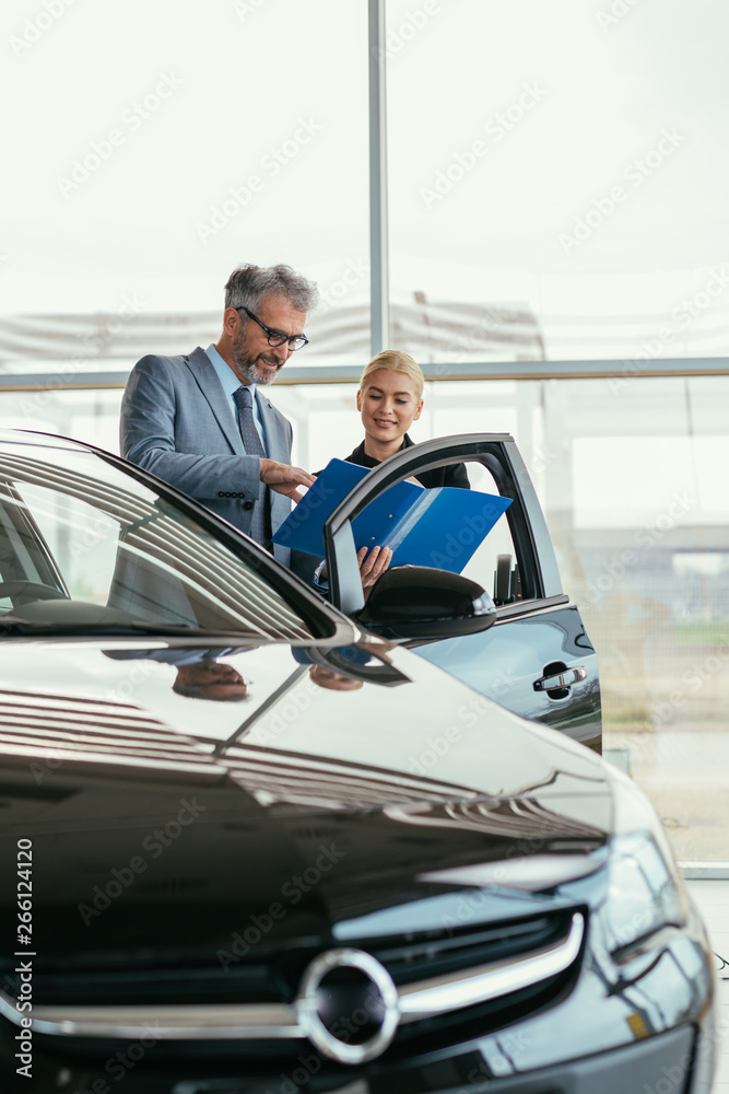 senior sales agent showing car brochure to customer in car dealers showroom senior sales agent showing car brochure to customer in car dealers showroom
