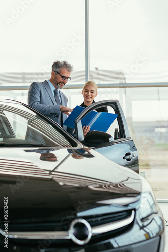 senior sales agent showing car brochure to customer in car dealers showroom