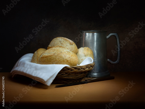 Bread and ale, rustic lunch, with old pewter tankard, bread rolls and knife. Painting like chiaroscuro still life. photo