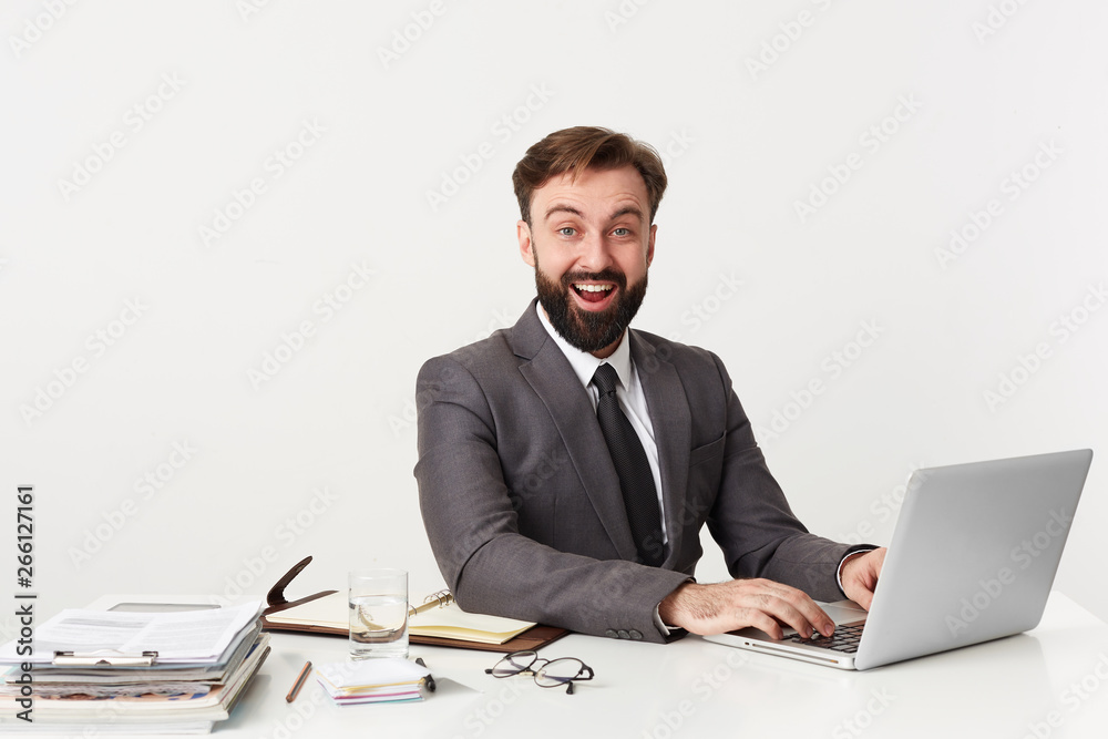 Portrait of an office top manager who smiles broadly because he heard a funny joke, sitting at desktop in office, working for his laptop , dressed in an expensive suit with a tie, enjoy his work. Portrait of an office top manager who smiles broadly because he heard a funny joke, sitting at desktop in office, working for his laptop , dressed in an expensive suit with a tie, enjoy his work.