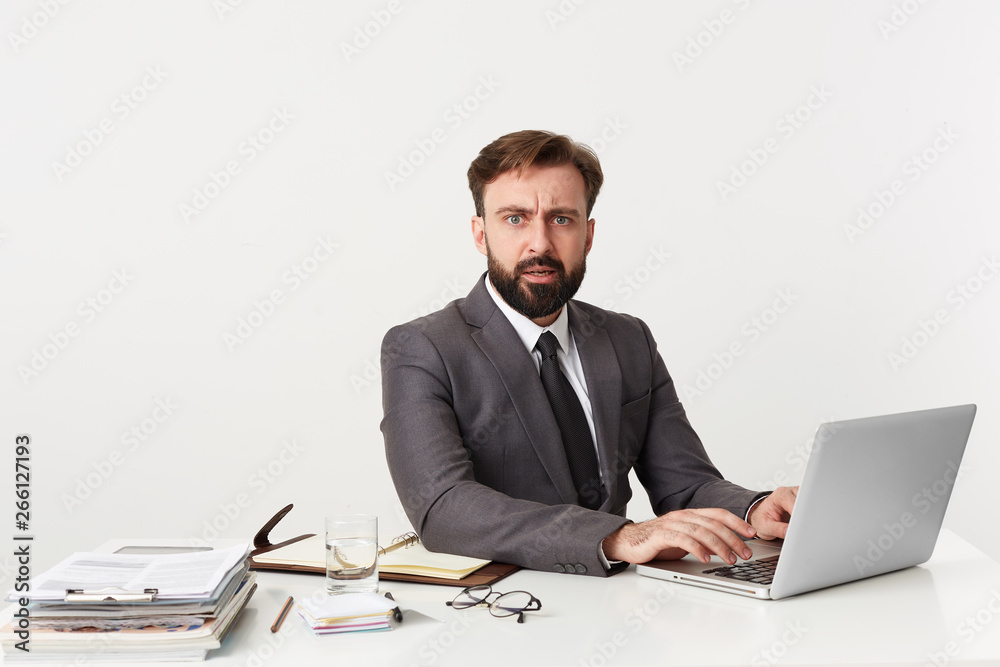 Portrait of an outraged office top manager who was distracted from work, sitting at desktop in office, working for his laptop , dressed in an expensive suit with a tie. Portrait of an outraged office top manager who was distracted from work, sitting at desktop in office, working for his laptop , dressed in an expensive suit with a tie.