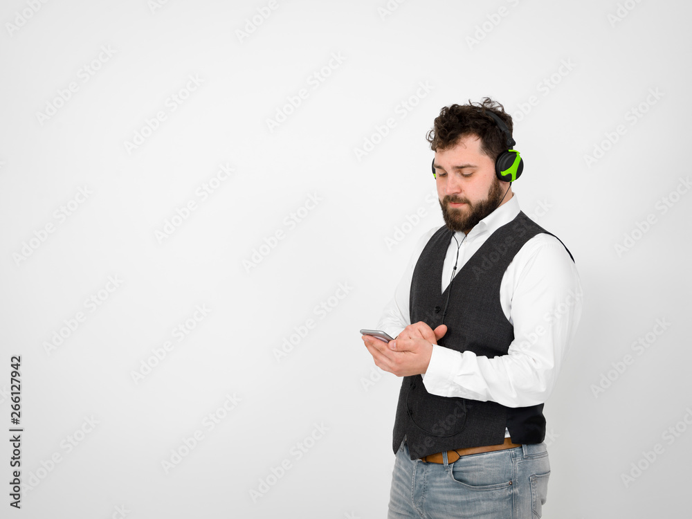 cool man with black beard and white shirt is posing with headphones and smartphone in front of white background cool man with black beard and white shirt is posing with headphones and smartphone in front of white background