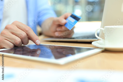 Young man sitting in office and pays by credit card with his tablet.