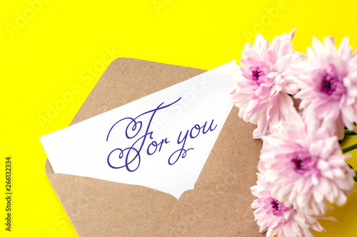 Love envelope and letter with written words for you with pink chrysanthemum flowers on bright yellow bacground.