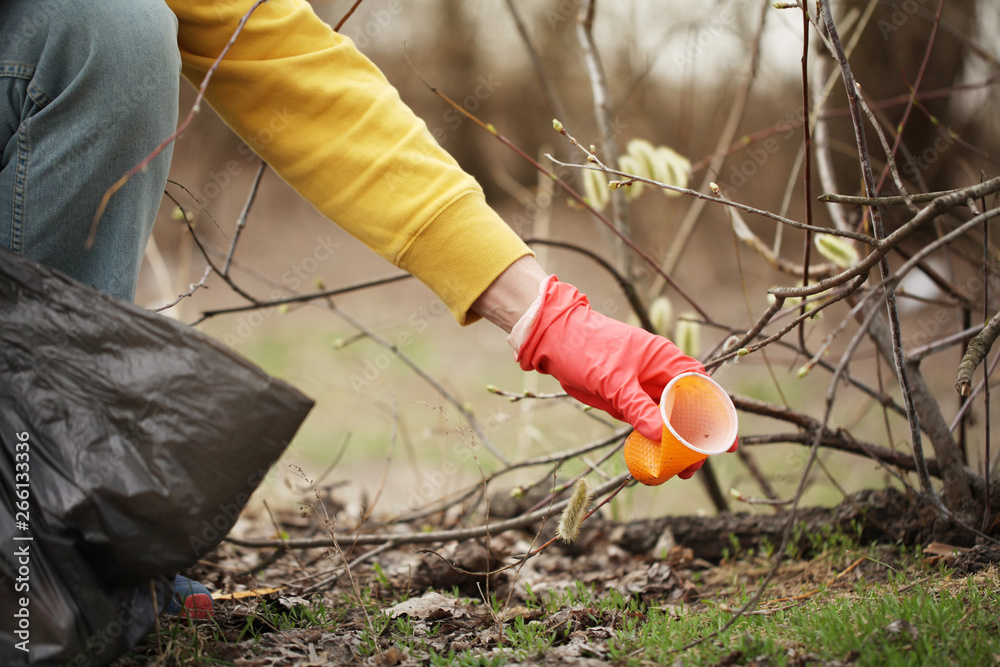 Obraz premium Hand of volunteer lift off litter ground. Spring cleaning in nature, outdoor trash and rubbish.