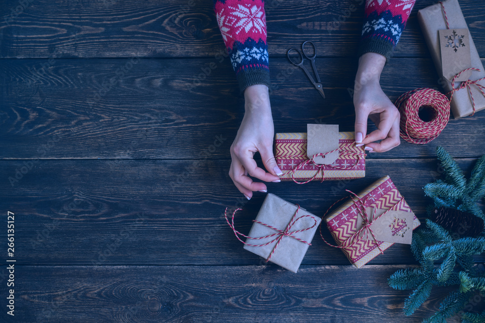 Obraz premium Christmas and New Year holiday background. Female hands holding rustic decorated Christmas gift box wrapped craft paper with twine. Traditional preparation for winter holidays. Toned image. Soft focus