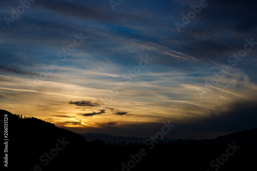 Sunset in a mystic scenery with colorful sunset with different types of clouds and a hill silhouette in the austrian alps in styria