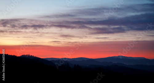 colorful sunset with glowing clouds and a tree a hill and valley silhouette in the austrian alps