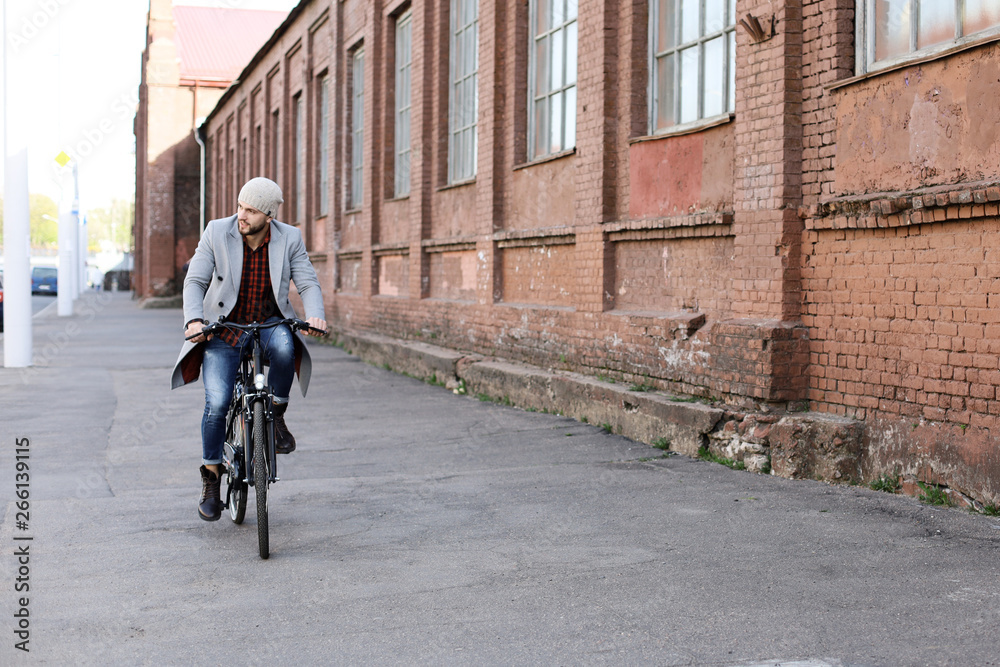 Handsome young man in grey coat and hat riding a bicycle street in the city.