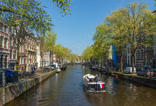 Outdoor sunny view of typical Holland brick architectures, sailing boats and street along beautiful shady canal in spring season in the morning.