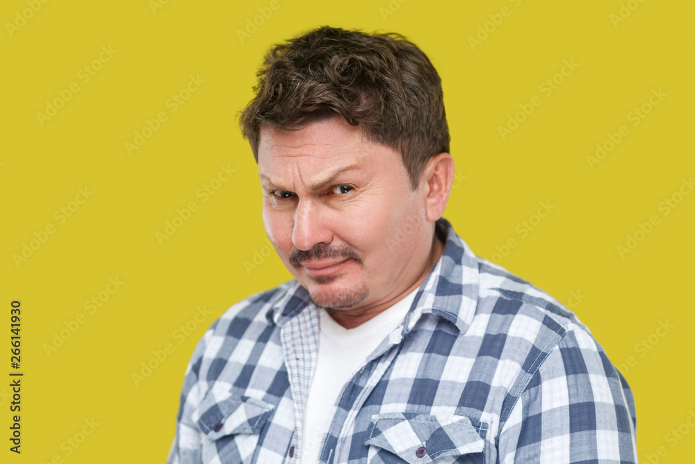 Fototapeta premium closeup portrait of serious handsome middle aged business man in casual checkered shirt standing and looking at camera with doubtful face. indoor studio shot, isolated on yellow background.