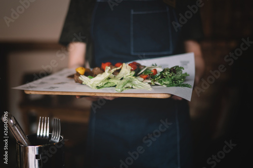 Waiter serving salad and grilled meat at restaurant, close up view. Eating and leisure concept. Toned image. Selective focus.