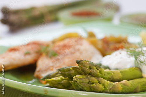 Roasted chicken breast meat and asparagus with sauce on green plate. Asparagus meal decorated with lemon and dill. Homemade cuisine. Close up image, shallow depth of field.