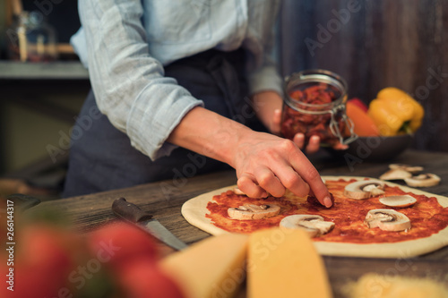 Fresh pizza with tomato and mushrooms. Homemade tasty pizza on dark wooden background. Raw dough for pizza with ingredients and spices on wooden rustic table. Traditional Italian food. Soft focus.