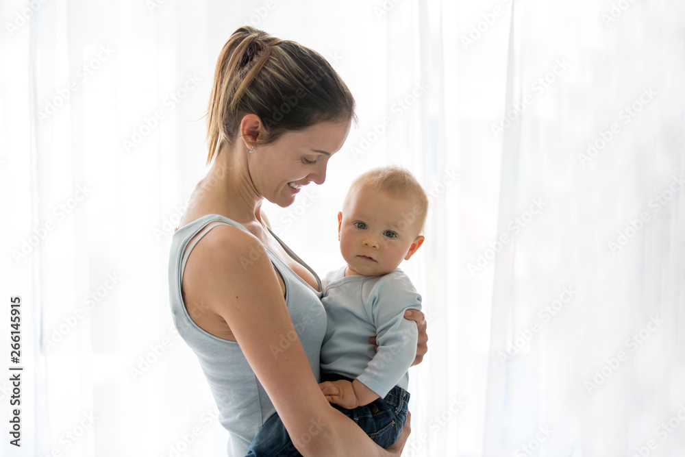 Young mother, embracing with tenderness and care her baby boy, smiling happilye Young mother, embracing with tenderness and care her baby boy, smiling happilye