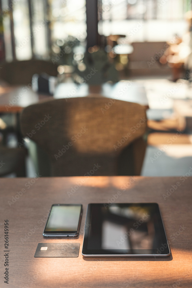 Modern digital smartphone and tablet computer with credit card lying on wooden table in cafe