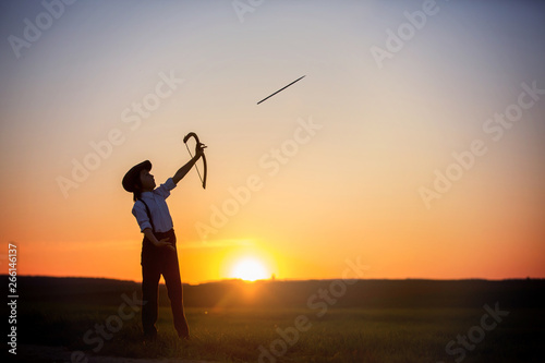 Silhouette of child playing with bow and arrows, archery shoots a bow at the target.