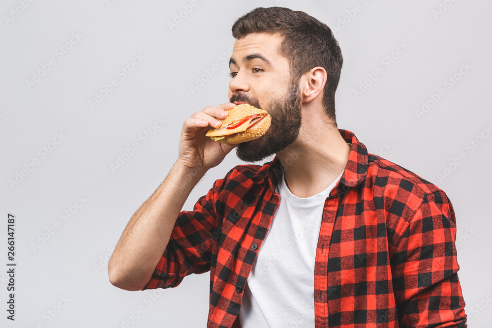 Young man holding a piece of hamburger. Student eats fast food. Burger is not helpful food. Very hungry guy. Diet concept isolated against white background. Young man holding a piece of hamburger. Student eats fast food. Burger is not helpful food. Very hungry guy. Diet concept isolated against white background.