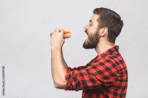 Young man holding a piece of hamburger. Student eats fast food. Burger is not helpful food. Very hungry guy. Diet concept isolated against white background.