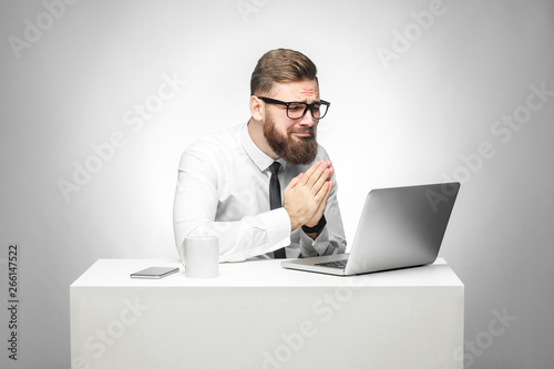 Foto I need your help! Portrait of hopeful bearded young manager in white shirt and black tie are sitting in office and talking with friend thought skype and pleased for helping him in work task