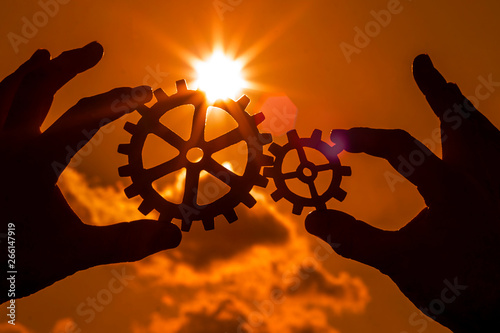 gears in the hands of people on the background of the evening sky. mechanism. interaction.