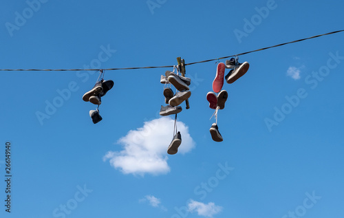 Many pairs of sports shoes hung on a rope against a blue sky.