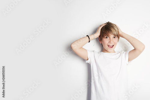 Handsome young boy in white T-shirt posing in front of white empty wall. Concept of children style and fashion. Mock-up.