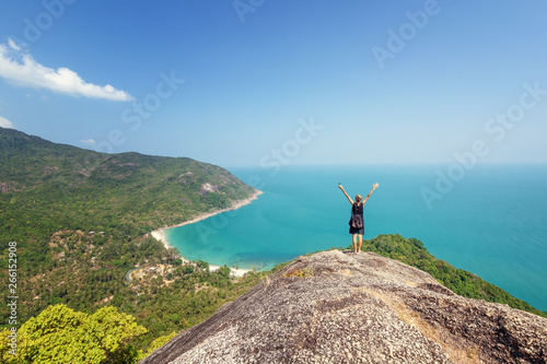 Young woman worth of grief and looks at beautiful bright blue sea, back view. Hands up. Adventure wanderlust lifestyle