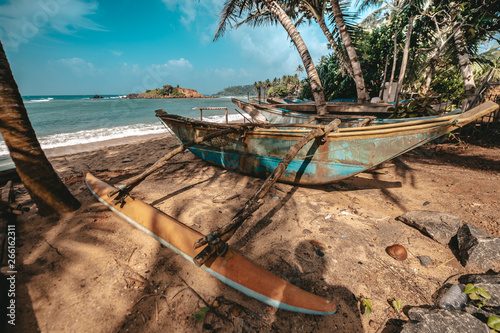 Asian fishing boats on the sand near palm trees on the shore of Indian Ocean with blue sky and clouds