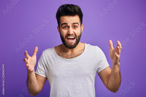 young angry bearded man expresses his negative emotions, having an argument with somebody, isolated blue background,
